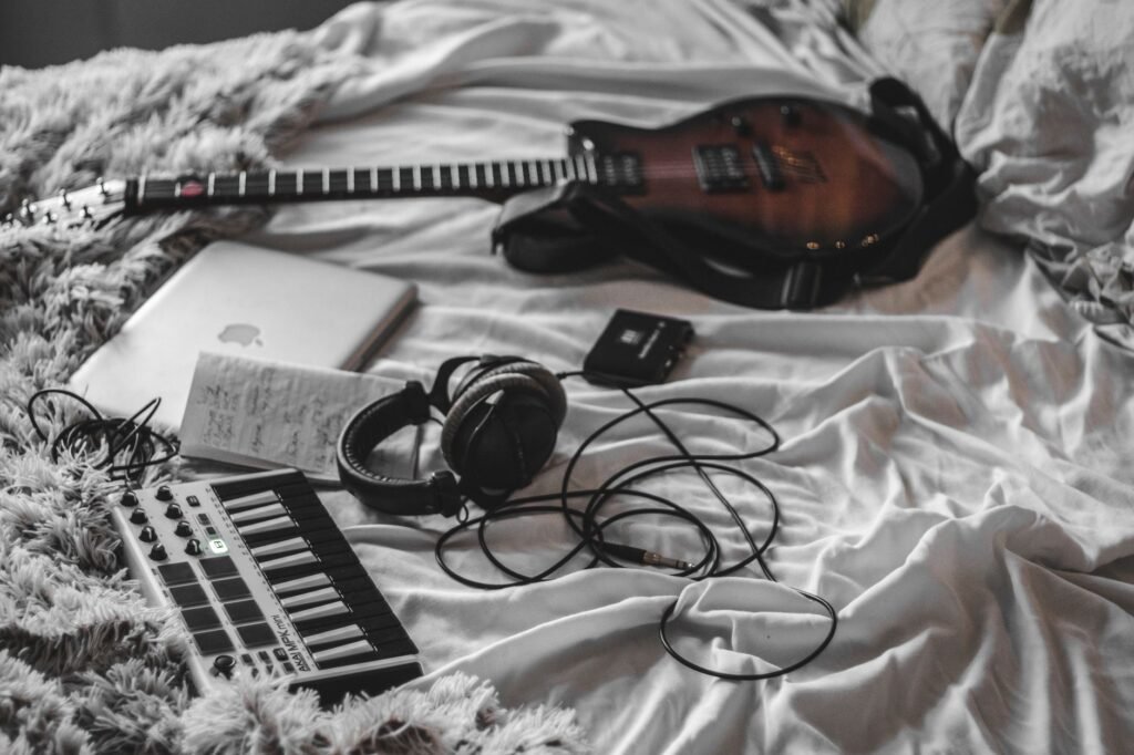 Hands on a MIDI keyboard beside a laptop and wired headphones in a small recording setup.